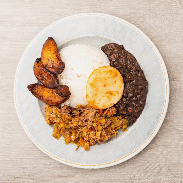 A plate of white rice, black beans, shredded beef, fried plantains, and a corn cake.