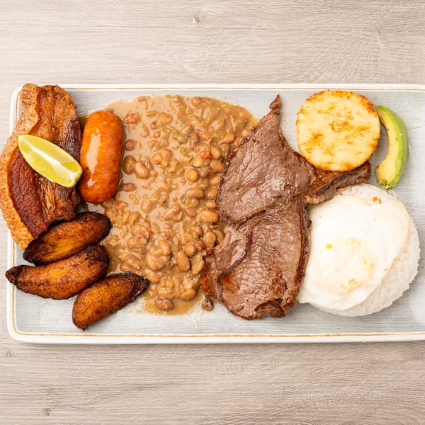 A bandeja paisa with steak, chicharron, chorizo, beans, rice, fried egg, plantains, avocado, and lime.