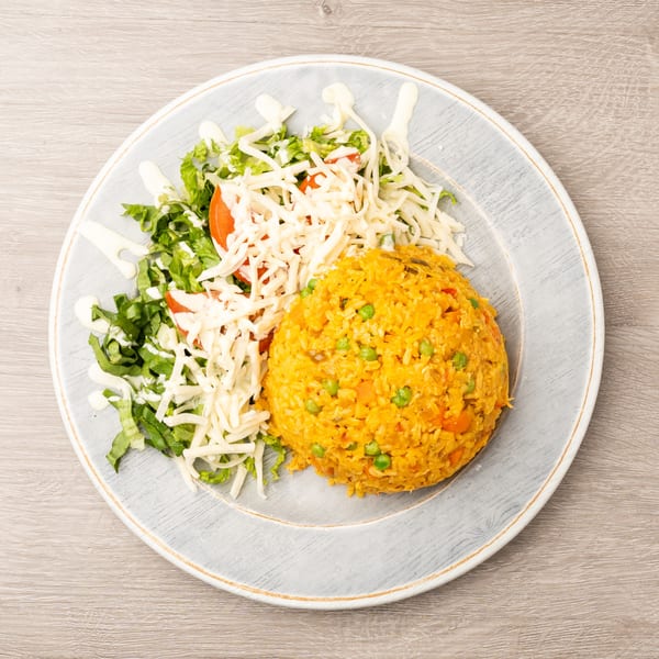 A plate of yellow rice with peas and carrots, alongside a fresh salad with shredded cheese and dressing.