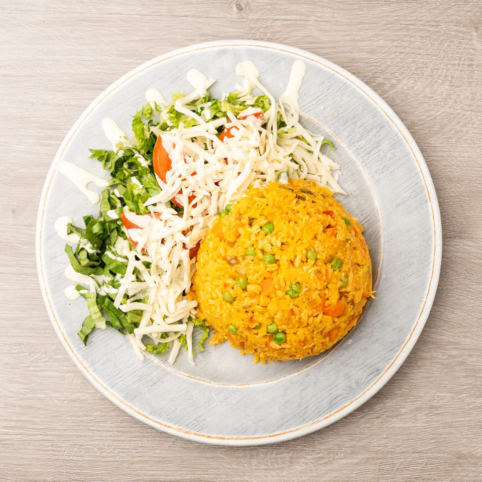 A plate of yellow rice with peas and carrots, alongside a fresh salad with shredded cheese and dressing.