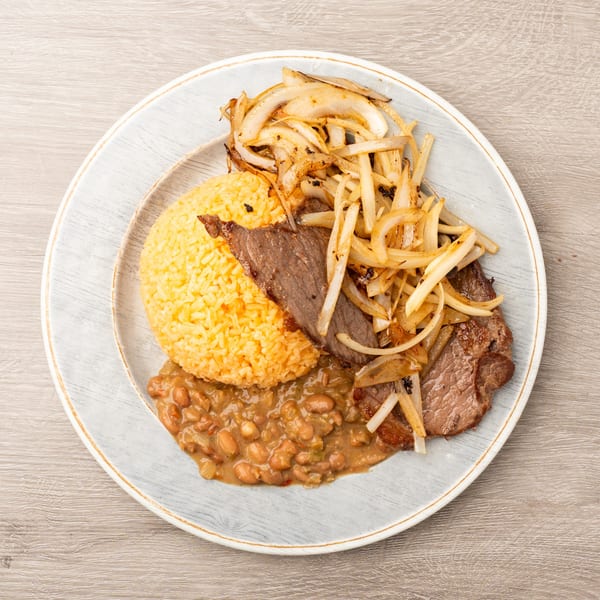 Steak with sautéed onions, yellow rice, and pinto beans on a white plate.