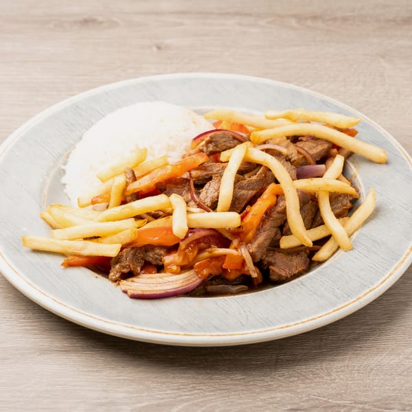 Lomo Saltado with steak, red onions, tomatoes, french fries, and white rice on a gray plate.