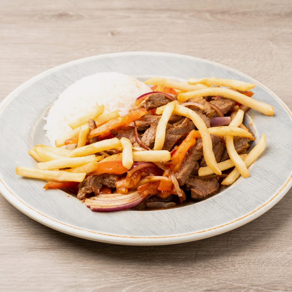 Lomo Saltado with steak, red onions, tomatoes, french fries, and white rice on a gray plate.