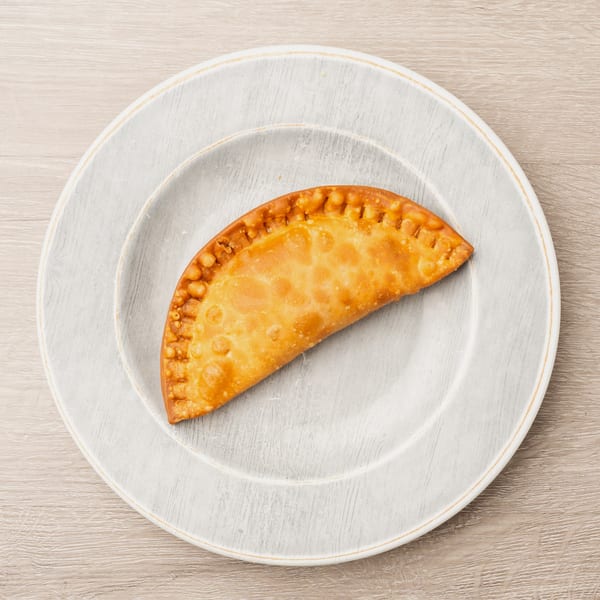 Golden brown empanada with crimped edges on a light gray plate, on a wooden table.