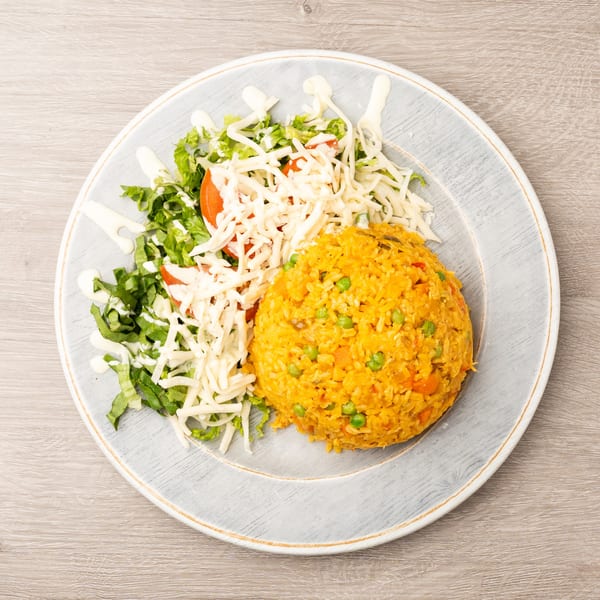 A plate of yellow rice with peas and carrots, alongside a fresh salad topped with shredded cheese and dressing.