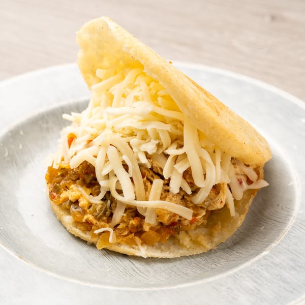 A golden arepa filled with shredded chicken and topped with a generous amount of white shredded cheese.