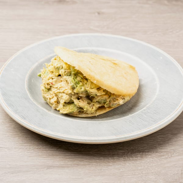 A golden-brown arepa filled with creamy chicken and avocado salad, served on a light gray plate.