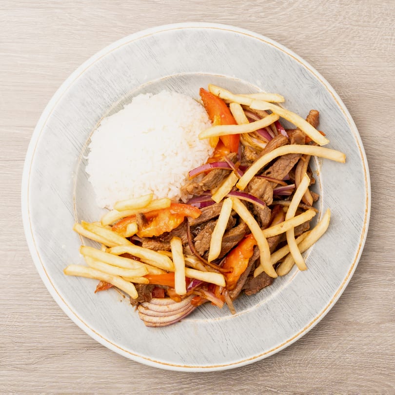 Lomo Saltado with beef, red onions, tomatoes, french fries, and white rice on a gray plate.