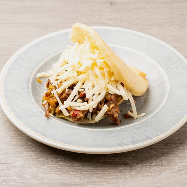 Arepa stuffed with shredded beef and cheese, served on a light blue plate.