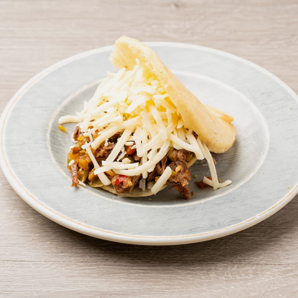 Arepa stuffed with shredded beef and cheese, served on a light blue plate.