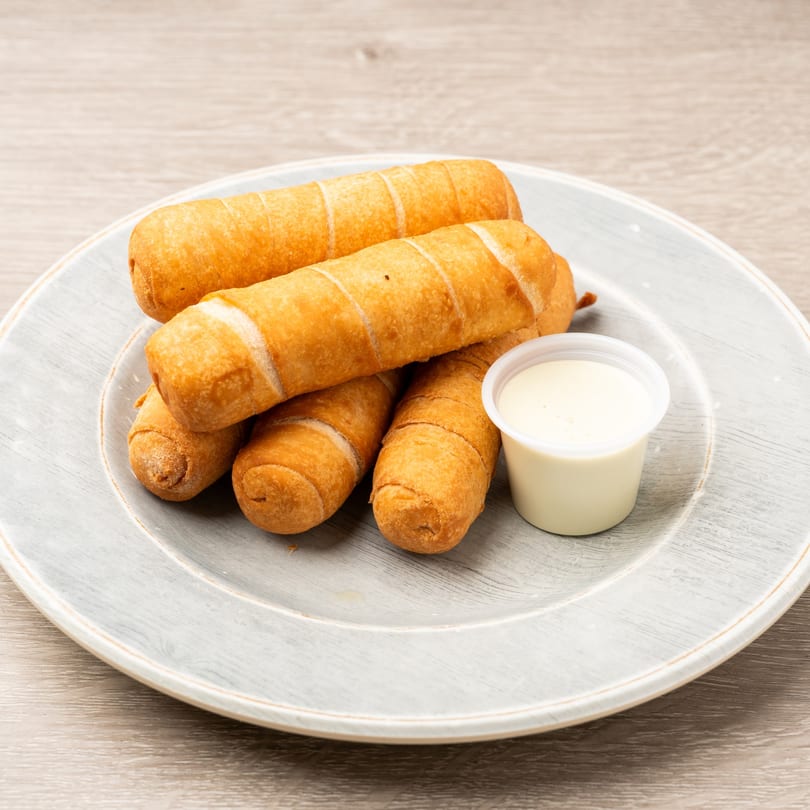 Golden-brown fried cheese sticks, called Tequeños, are served on a gray plate with a side of white dipping sauce.